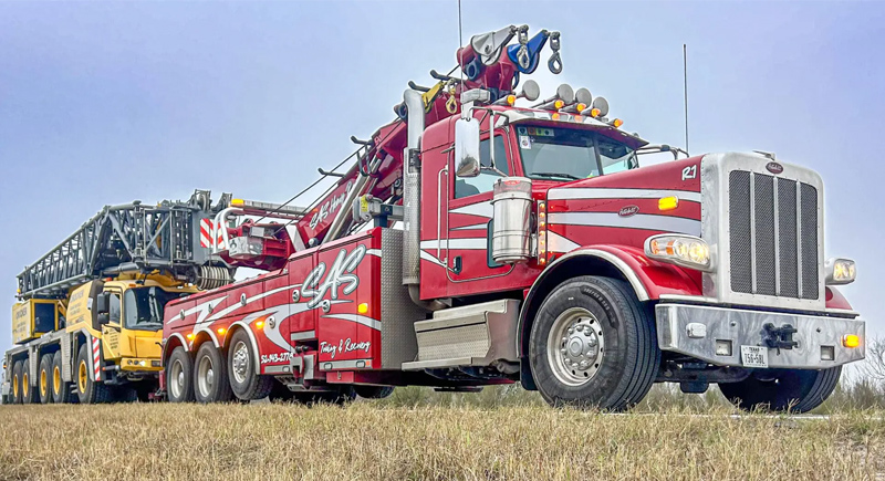 Heavy-duty rotator tow truck transporting a large mobile crane along a roadside
