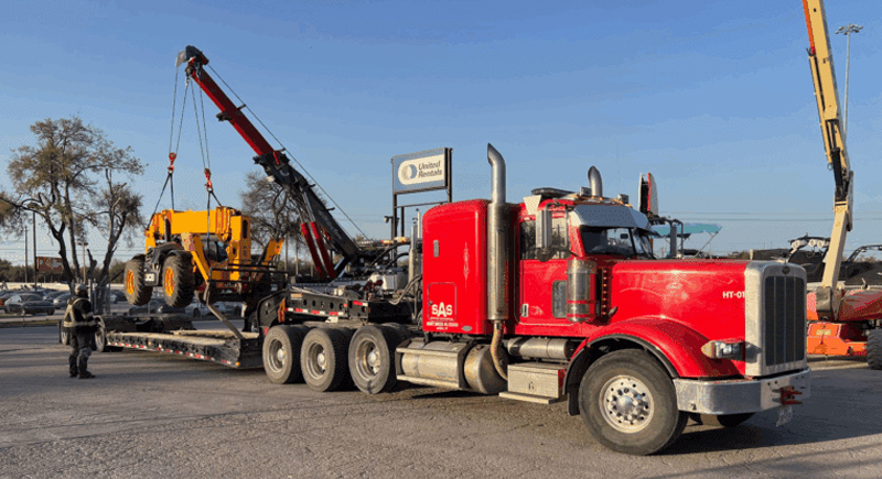 Boom crane truck lifting a telehandler onto a lowboy trailer for transport